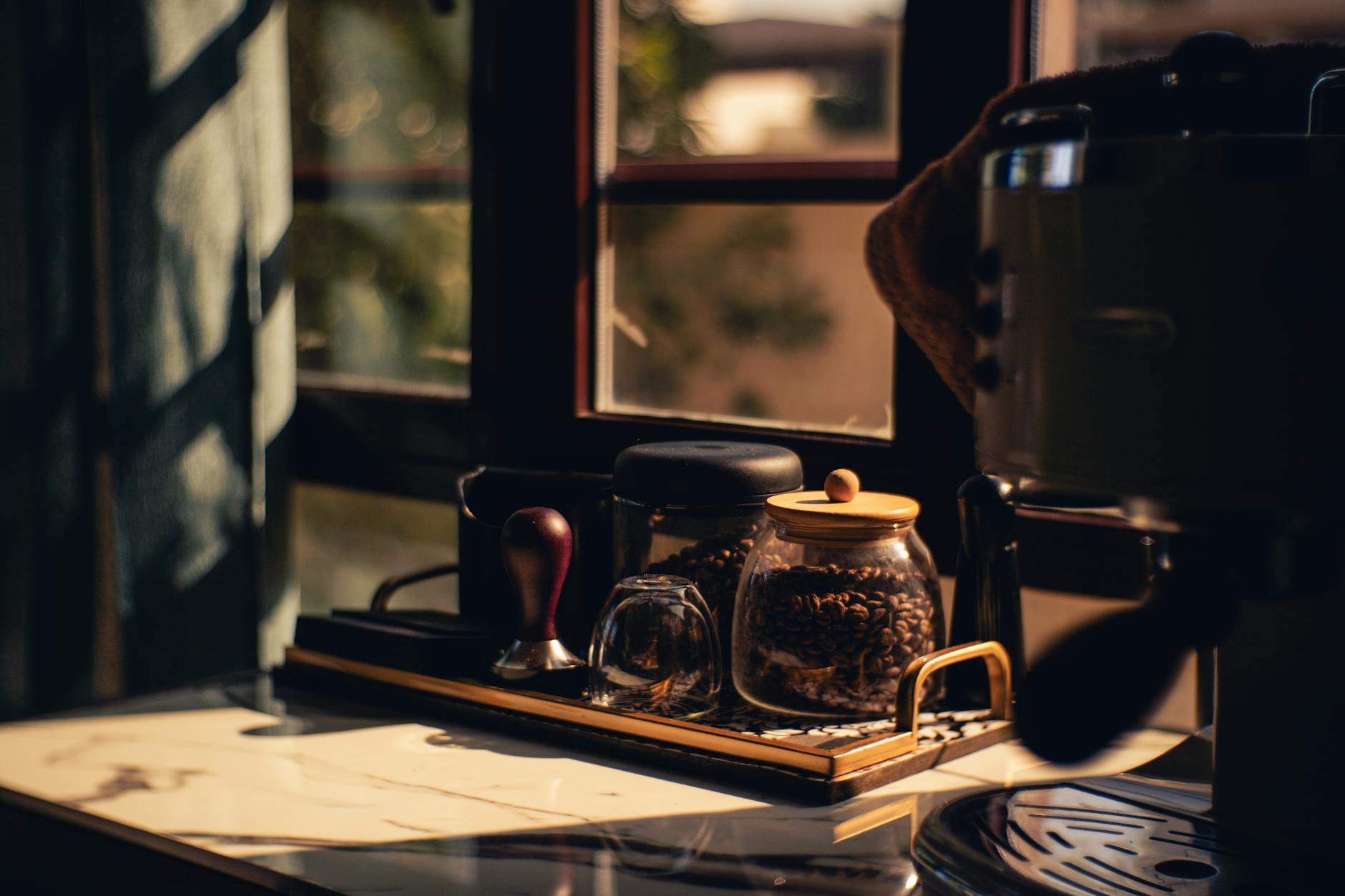 Kącik kawowy przy oknie z ekspresem i słoikami na kawę w porannym słońcu