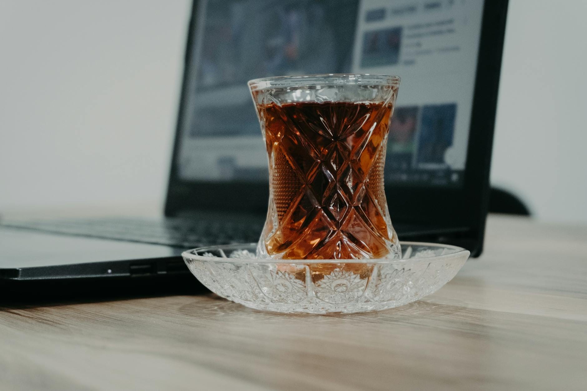 Szklanka czarnej herbaty obok otwartego laptopa na drewnianym biurku
