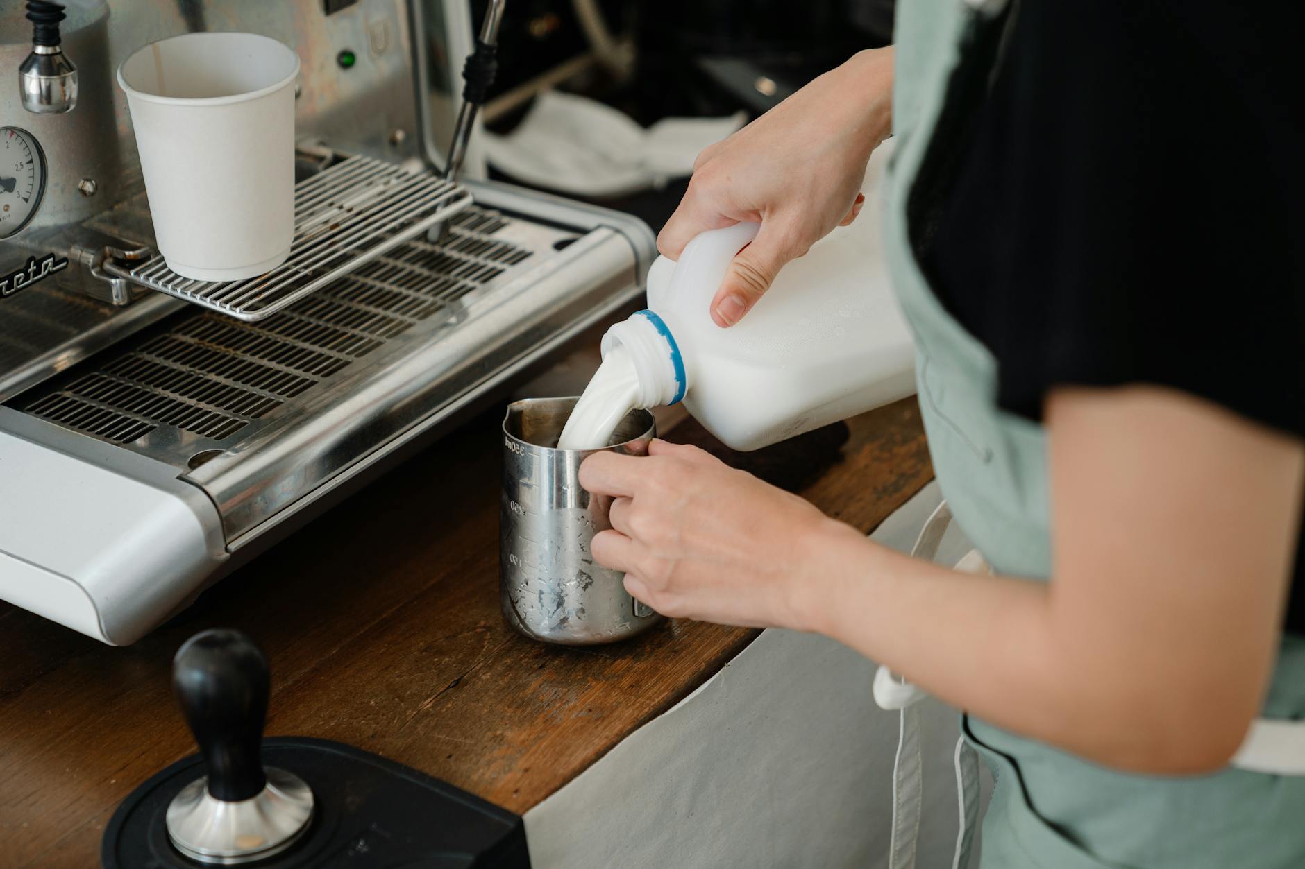 Barista w kawiarni wlewa świeże mleko do metalowego dzbanka przy ekspresie