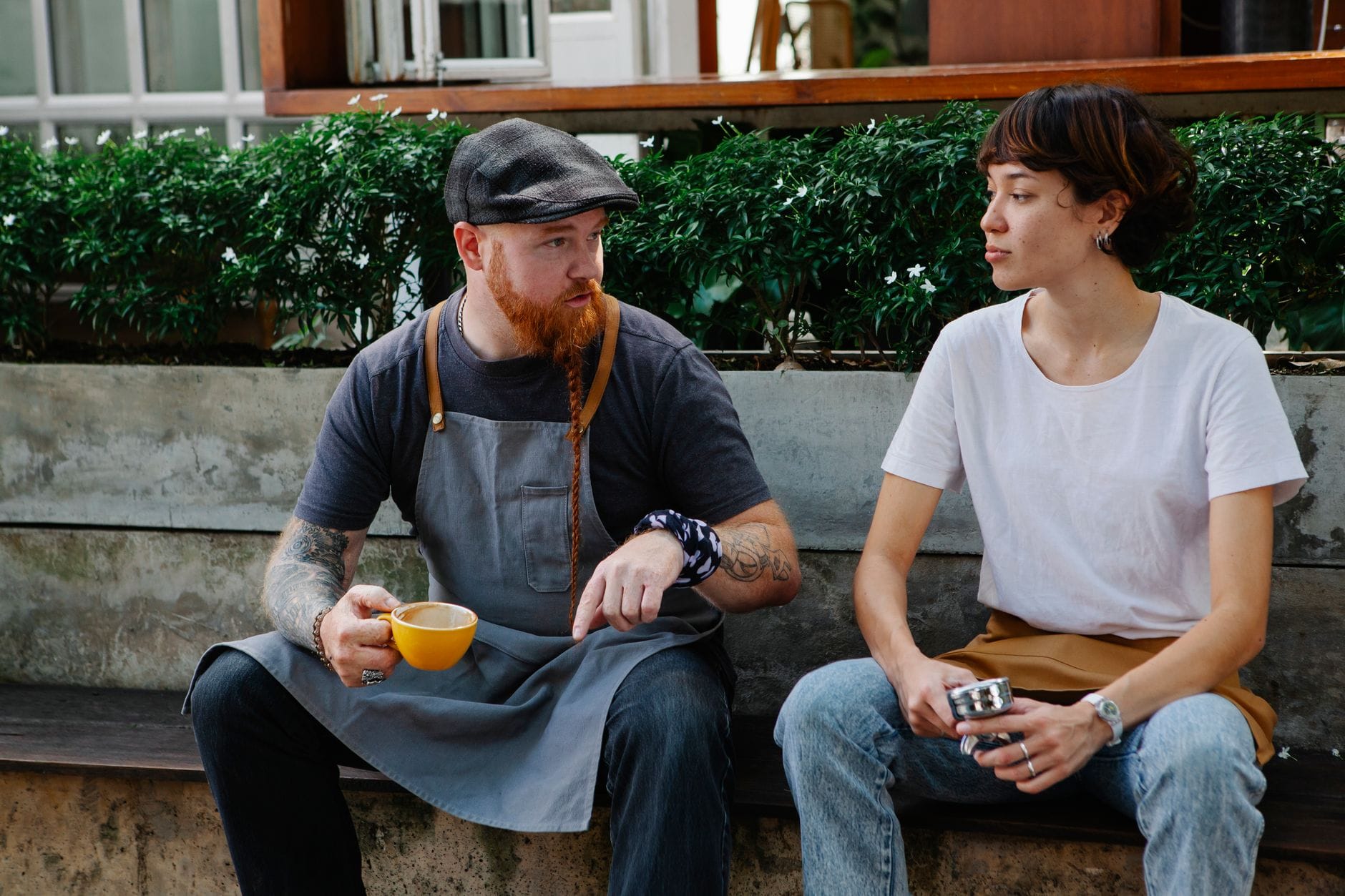 Baristka i barista przed kawiarnią rozmawiają przy filiżance kawy