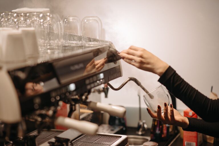 Barista spienia mleko dyszą parową ekspresu do kawy